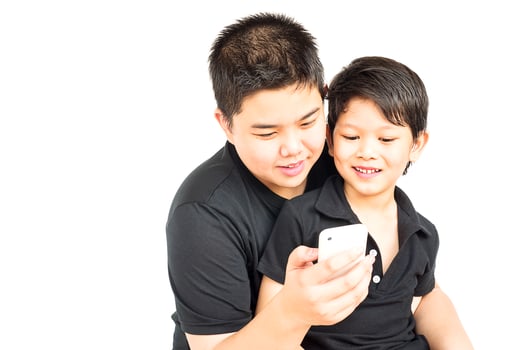 14 and 7 years Asian kids are happily looking at mobile  phone together isolated over white photo
