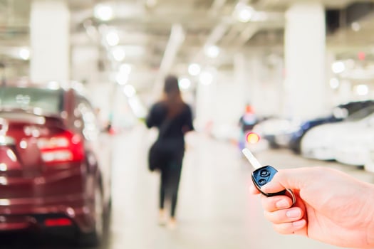 Hand is using car remote over blurred photo of a woman is walking dangerously in a car parking area