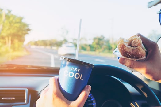 Man is dangerously eating hot dog and cold drink while driving a car photo