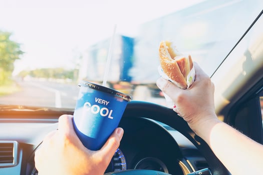 Man is dangerously eating hot dog and cold drink while driving a car photo