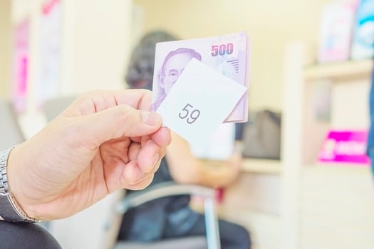 Man is holding queue card with 500 Baht Thai bank note while waiting in the modern bank reception area photo