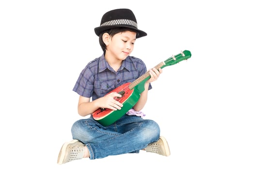 7 years old Asian boy is sitting and playing ukulele isolated over white. photo