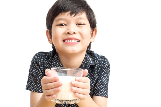 Asian boy is drinking a glass of milk over white background. Photo is focused at his hand.