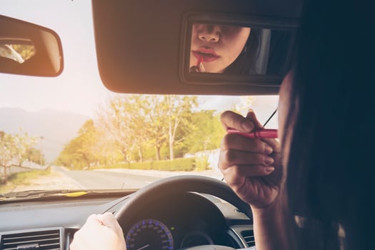 Woman making up her face using lipstick while driving car, unsafe behavior photo