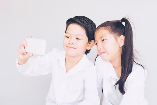 Lovely Asian couple school kids are taking selfie, 7 and 10 years old, over gray background photo