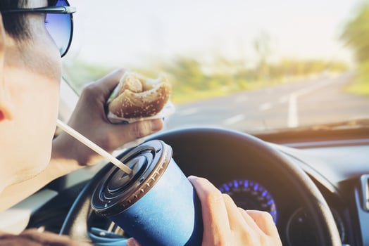 Man is dangerously eating hot dog and cold drink while driving a car photo