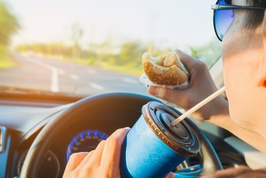 Man is dangerously eating hot dog and cold drink while driving a car photo