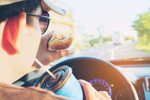 Man is dangerously eating hot dog and cold drink while driving a car photo