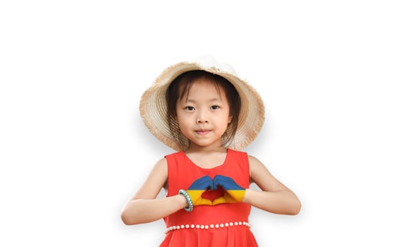 Little girl wear hat showing heart sign with his hands painted in Ukraine flag color isolated on white background. Stop the war for peace. Love Ukraine concept. photo