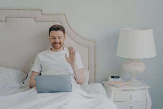 Relaxed young man with stubble using laptop laptop while sitting in bed photo