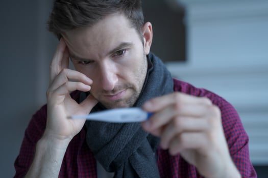Unhealthy sad young German businessman wearing scarf around neck looking at electronic thermometer photo