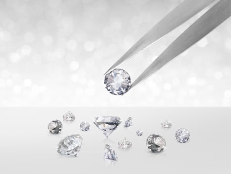 Diamond in tweezers on white shining bokeh background. concept for chossing best diamond gem design photo