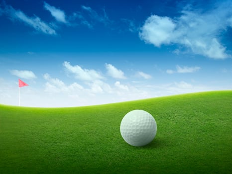 Close up golf ball on green grass field and red golf flag on green fairway with beautiful blue sky photo