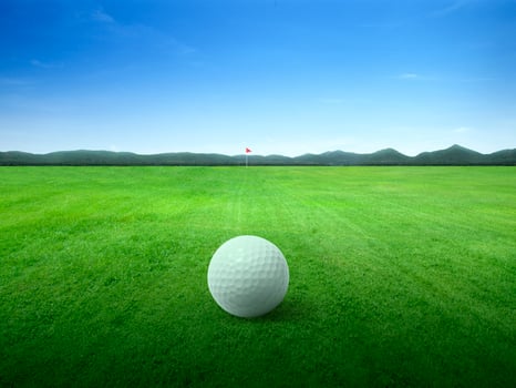 Close up golf ball on green grass field and red golf flag on green fairway with beautiful blue sky photo