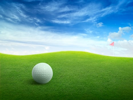 Close up golf ball on green grass field and red golf flag on green fairway with beautiful blue sky photo