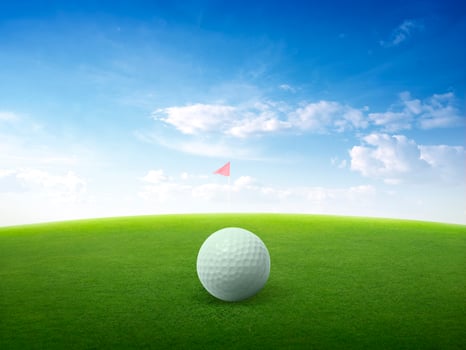 Close up golf ball on green grass field and red golf flag on green fairway with beautiful blue sky photo