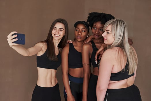 Making selfie. Group of multi ethnic women standing in the studio against brown background photo
