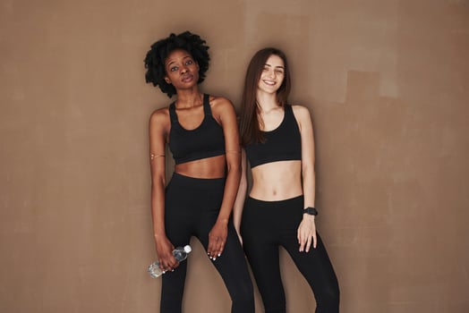 Relaxation after fitness workout. Two multi ethnic female friends stands in the studio with brown background photo