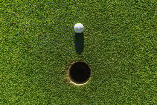 golf ball on green grass with hole and sunlight photo