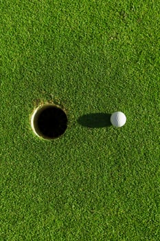 golf ball on green grass with hole and sunlight photo