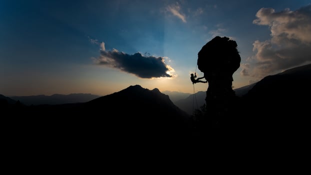 Silhouette of a rock climber descending on the rope after climbing at sunset photo