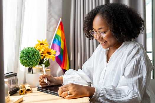 African girl is working at home with LGBTQ rainbow flag in her table for coming out of the closet and pride month celebration to promote sexual diversity and equality in homosexual orientation photo