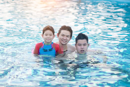 Father and his two son play in clear water swimming pool - happy family play time concept photo
