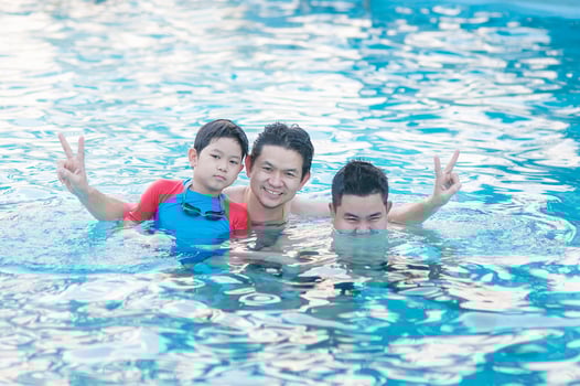 Father and his two son play in clear water swimming pool - happy family play time concept photo