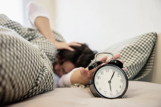 Sleepy woman reaching  holding the alarm clock in the morning with late wake up - every day life at home concept photo