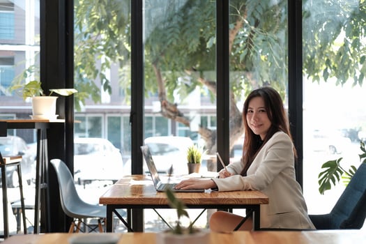 Side view young asian businesswoman sitting on her workplace in the office. Young woman working for financial document data charts with laptop in the office. photo