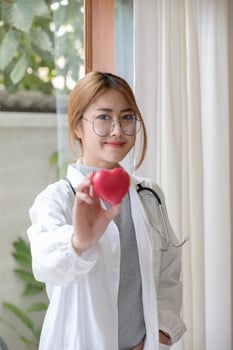Portrait young asian beautiful doctor with stethoscope holding heart while standing at her office. photo