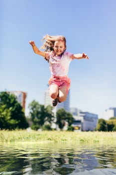 Little girl jumping high above big puddle of water. photo