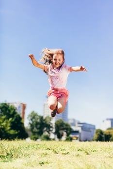 Little girl jumping high in the city park in colorful dirty clothes. photo