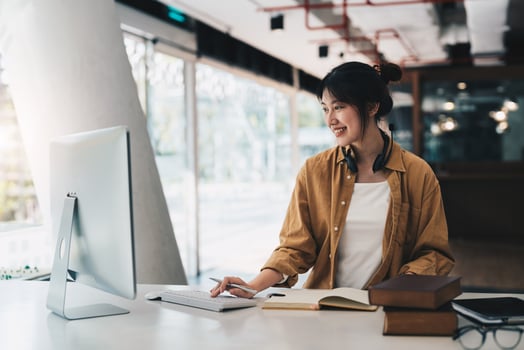 Hipster asian girl school student with wear headphone write notes watch video online webinar learn on laptop sit in bed distance elearning course video conference pc call in bedroom at home photo