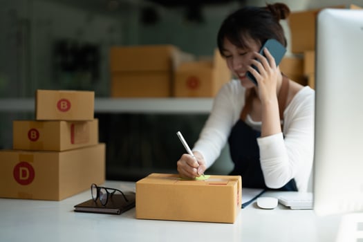 Young Asian small business owner working at home office, taking note on purchase orders. Online marketing packaging delivery, startup SME entrepreneur or freelance woman concept photo