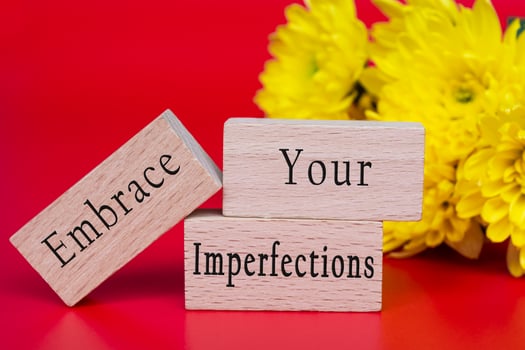 Embrace your imperfections text on wooden cube and with flowers background. photo