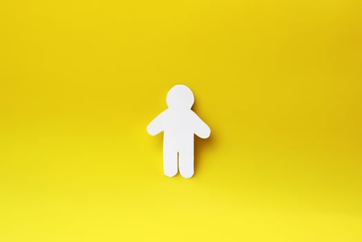 Silhouette of a man of white paper, cut by hand. In the center of the photo on yellow background