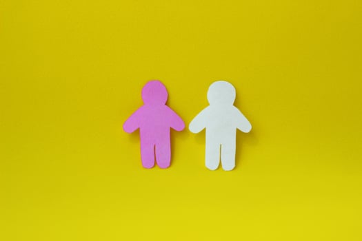 Two silhouettes of a people carved from white and pink paper on yellow background. photo