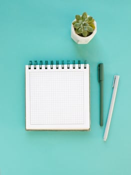 Top view of workspace and opened notebook with mock up blank pages on blue background. Flat lay photo
