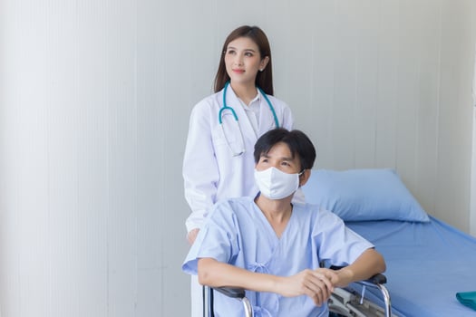 Asian doctor woman talking with a man patient who wear face mask about his health symptom while he sit on wheelchair at hospital. photo
