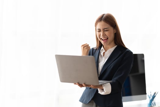 Portrait of an excited young asian business woman holding laptop computer and celebrating success isolated over white background, copy space. photo