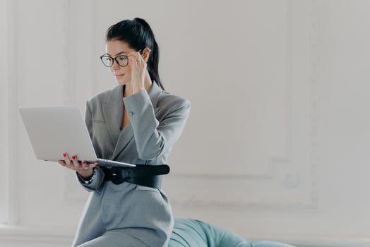Elegant professional woman banker concentrated at screen of laptop computer, dressed in formal wear, reads documents in online version poses in spacious room, home office. Business, technology concept photo