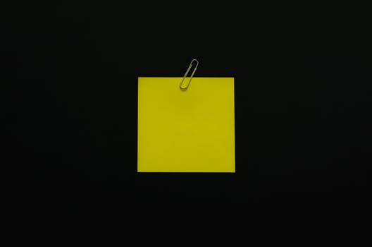 Yellow blank note paper with paper clip on dark background. Minimalist flat lay black concept. photo