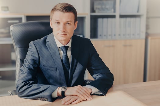 Professional male banker sits in cabinet, wears formal clothes, has confident expression while gives interview concerning banking, poses at office. Man employee arranges meeting of colleagues photo