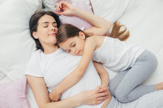Pleased little child sleeps near her mother, embraces with love, has pleasant dreams, lie on comfortable bed. Mum and cute daughter have good sleep in bedroom. Family, sleeping and rest concept photo