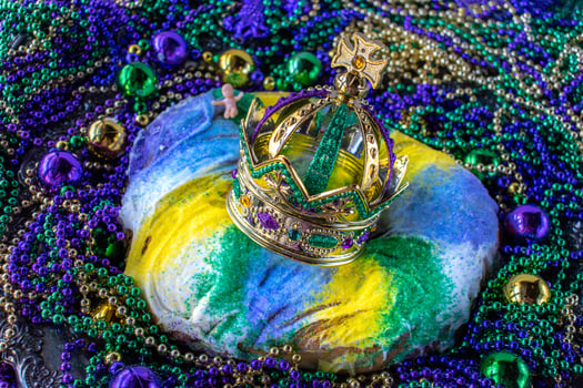Mardi Gras King Cake topped with crown surrounded by beads and decorations photo