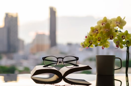 Spectacles put on open book with a cup of coffee, phalaenopsis orchid and city background. photo