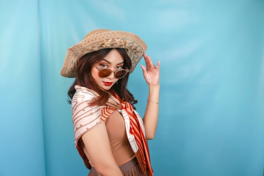 Young Asian confident and happy woman is glancing and holding her sunglasses isolated by a blue background. photo