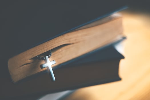 Closeup of wooden Christian cross necklace next to holy Bible photo
