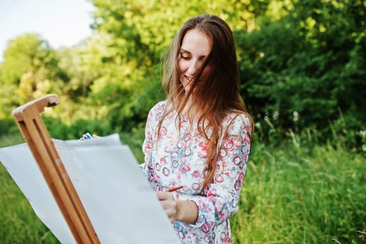 Portrait of an attractive young woman in long dress painting with watercolor in nature. photo